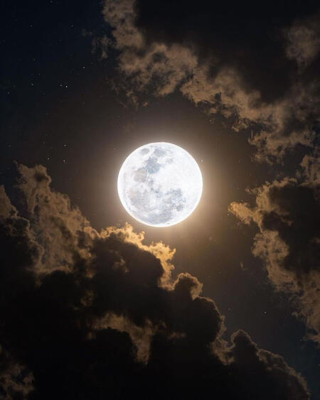 An image of a full moon surrounded by clouds. It has a warmer feel to the image.